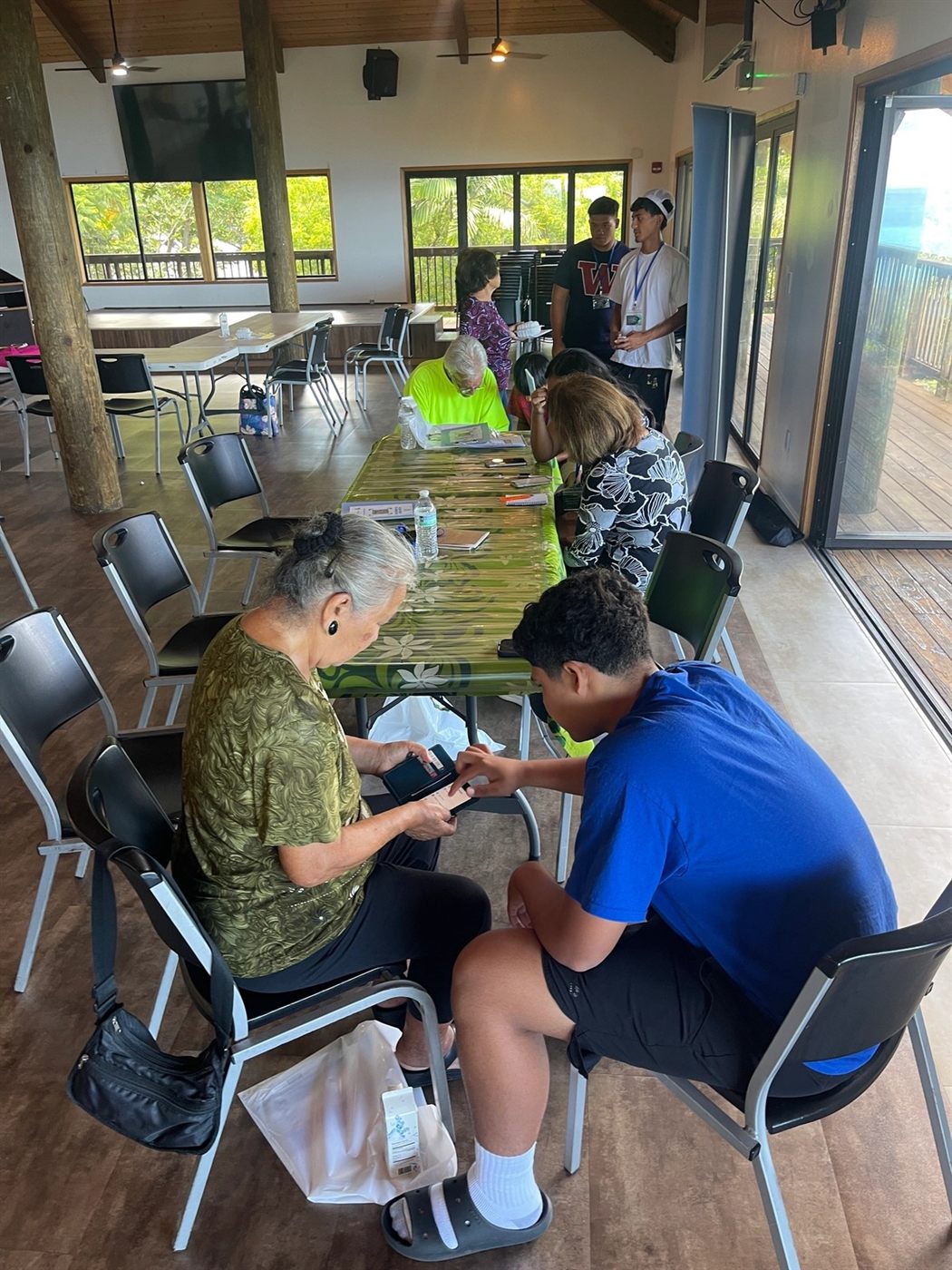 A Tech Savvy Teen sitting beside a kupuna, working through her smartphone with her at a community center table